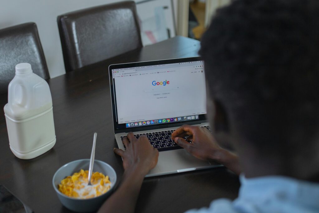 Imagem de um homem acessando o Google no computador e comendo cereal para ilustrar artigo sobre sites de busca na internet.
Imagem: Pexels. 