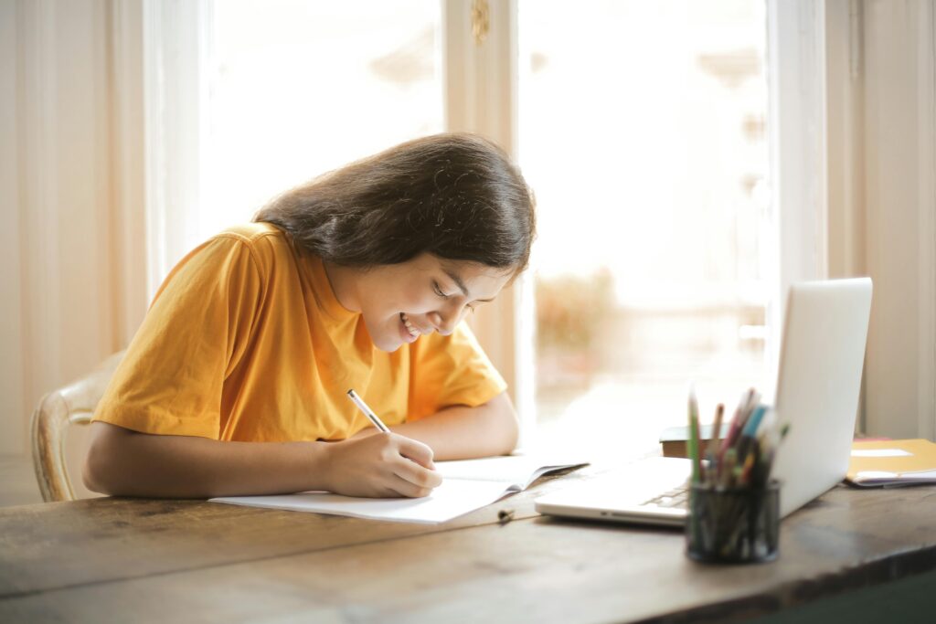 Mulher escrevendo em um caderno. Imagem: Pexels.