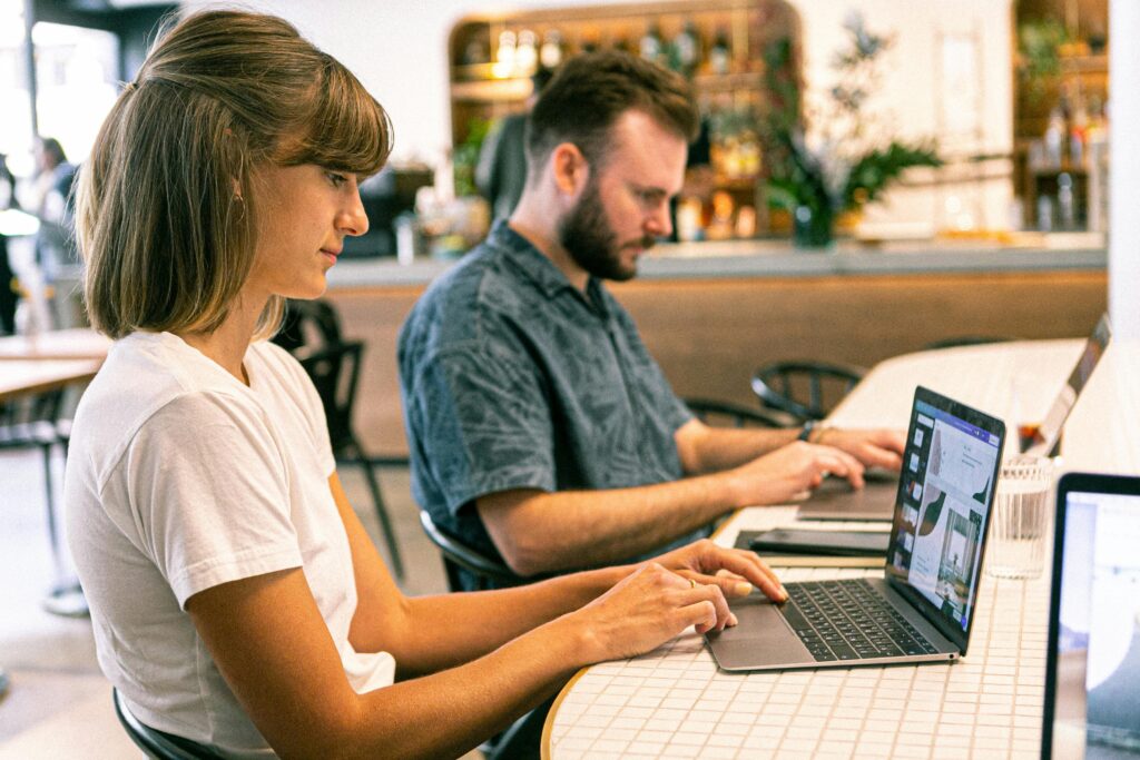 Um homem e uma mulher trabalhando lado a lado em frente aos seus notebooks. Imagem Pexels.