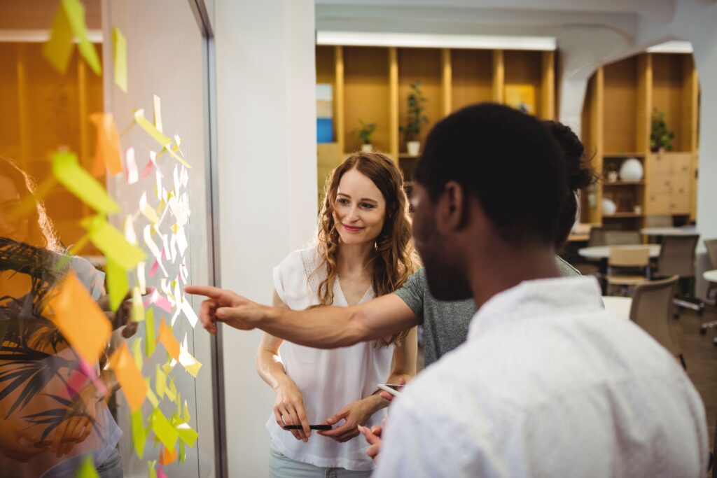 Imagem de três pessoas em ambiente de trabalho. Uma delas está apontando para um painel e conversando com as outras duas.
Foto: Freepík