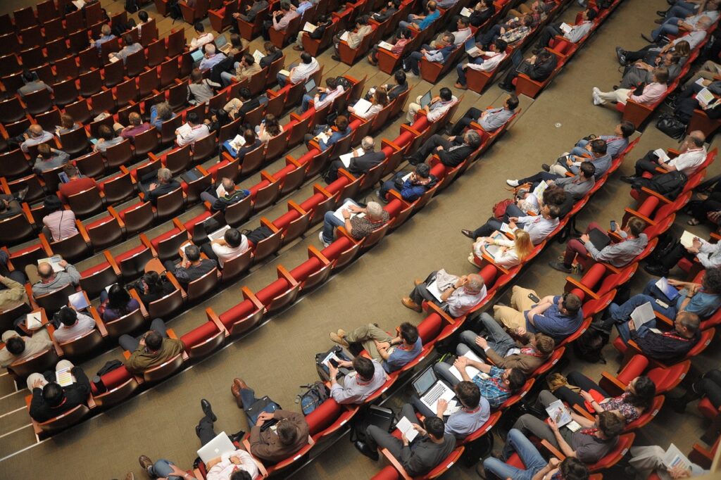 Imagem de um auditório ocupado por pessoas assistindo a um evento corporativo. Foto: Pixabay.